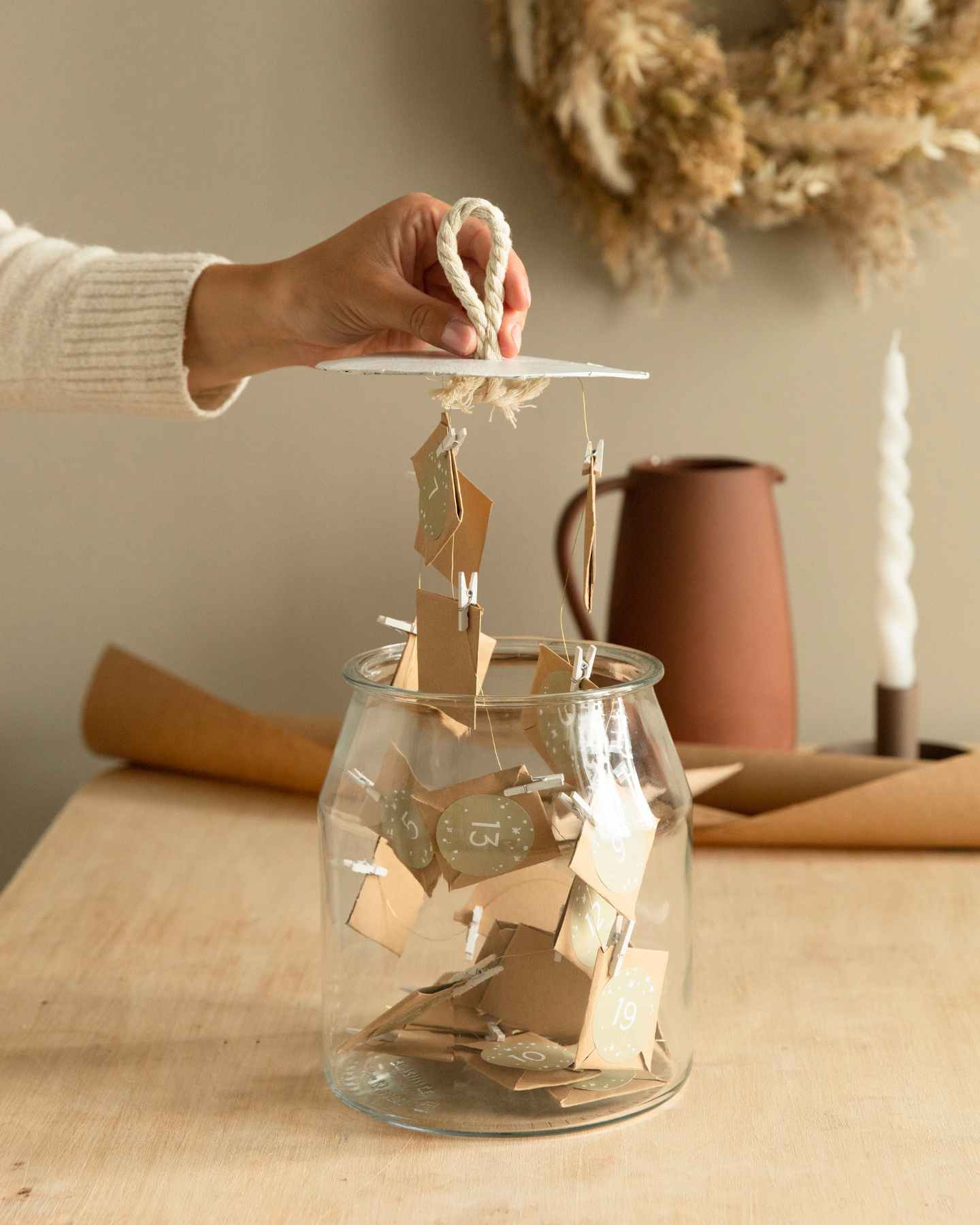 Frau hält Deckel aus Pappe an einer Schlaufe fest, an dem kleine Gutscheine aus Papier befestigt sind als Adventskalender.