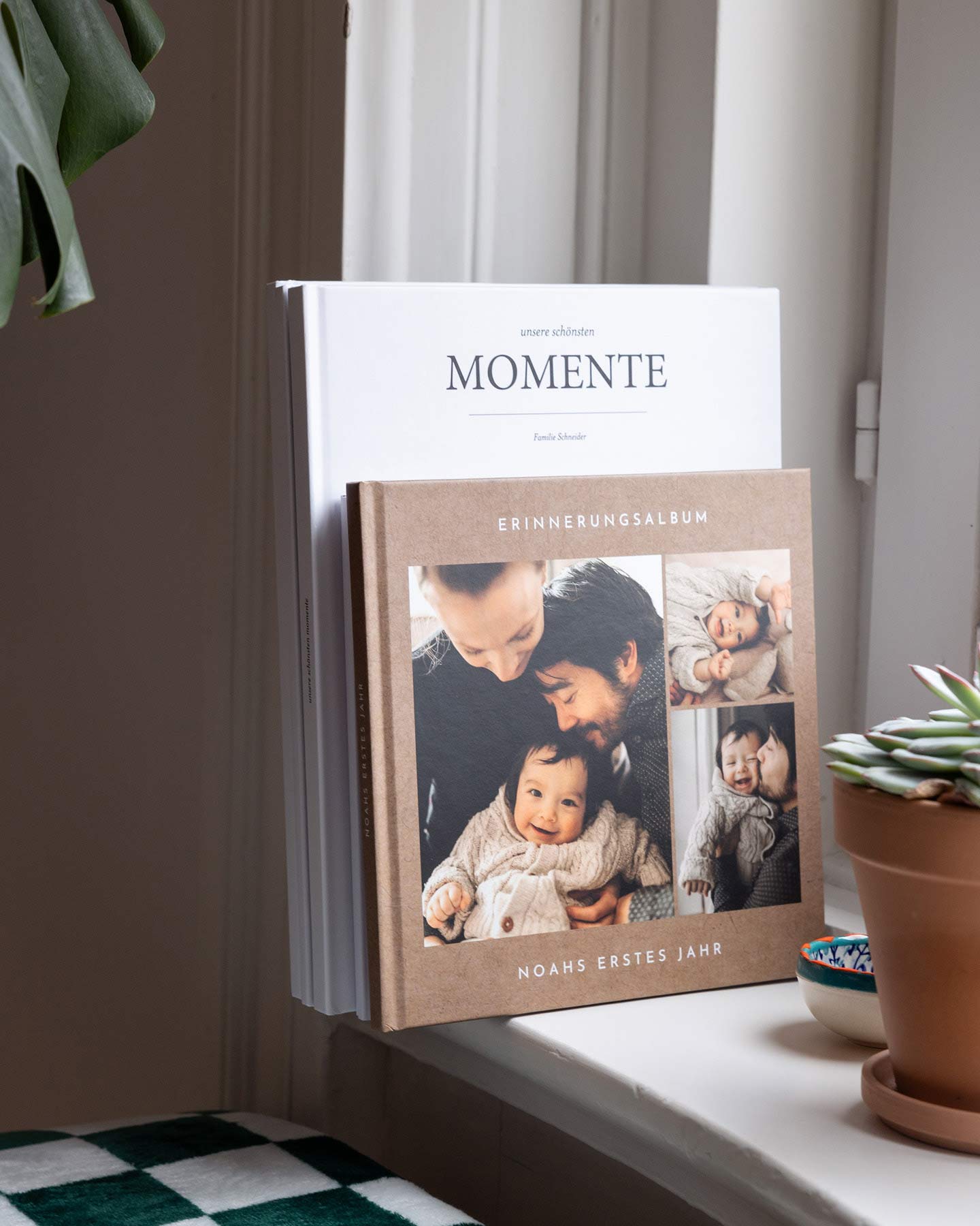 Zwei Fotobücher mit Fotos aus dem ersten Babyjahr stehen als Dekoration auf einem Fensterbrett