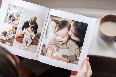 Frau hält Fotobuch mit Babybildern in den Händen und trinkt einen Kaffee