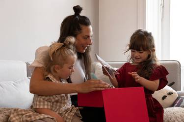 Frau auf der Couch mit 2 kleinen Mädchen öffnet ihr Weihnachtsgeschenk