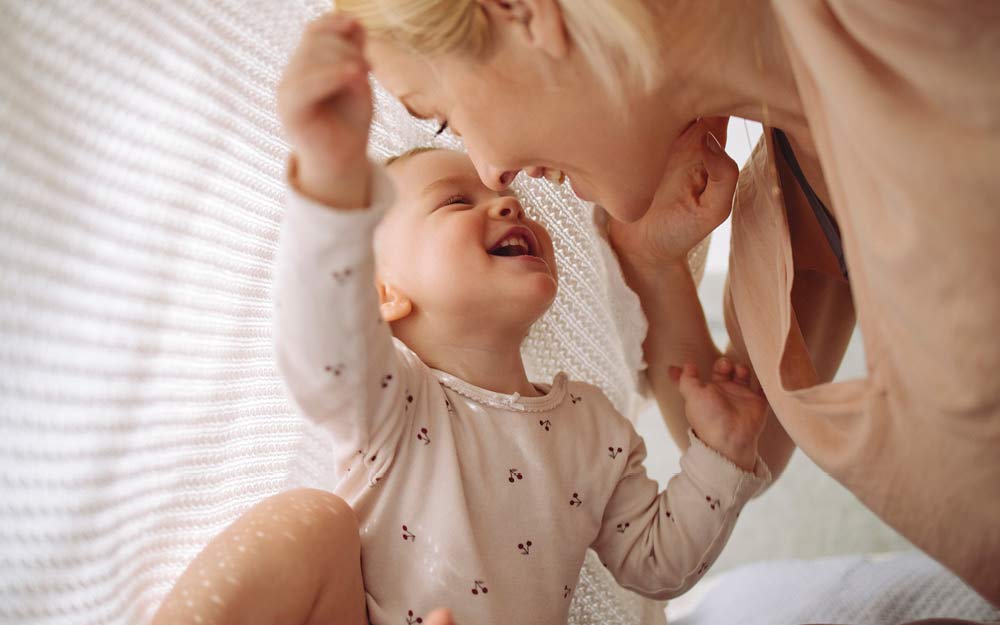 Mama und Baby sitzen auf dem Boden und lachen unter einer Decke