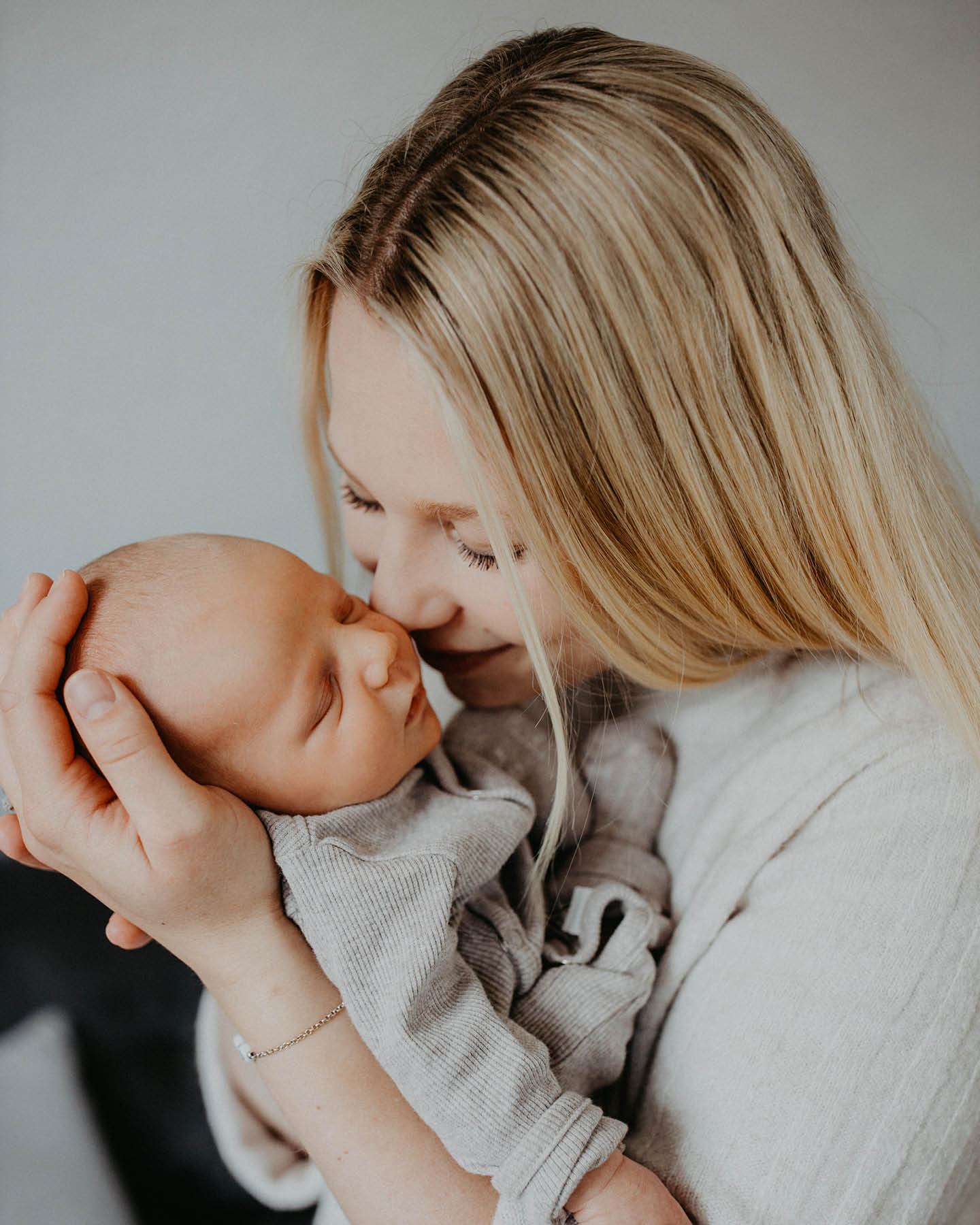 Mutter mit ihrem Neugeborenen auf dem Arm drückt ihre Nase zärtlich in die Wange des Babys