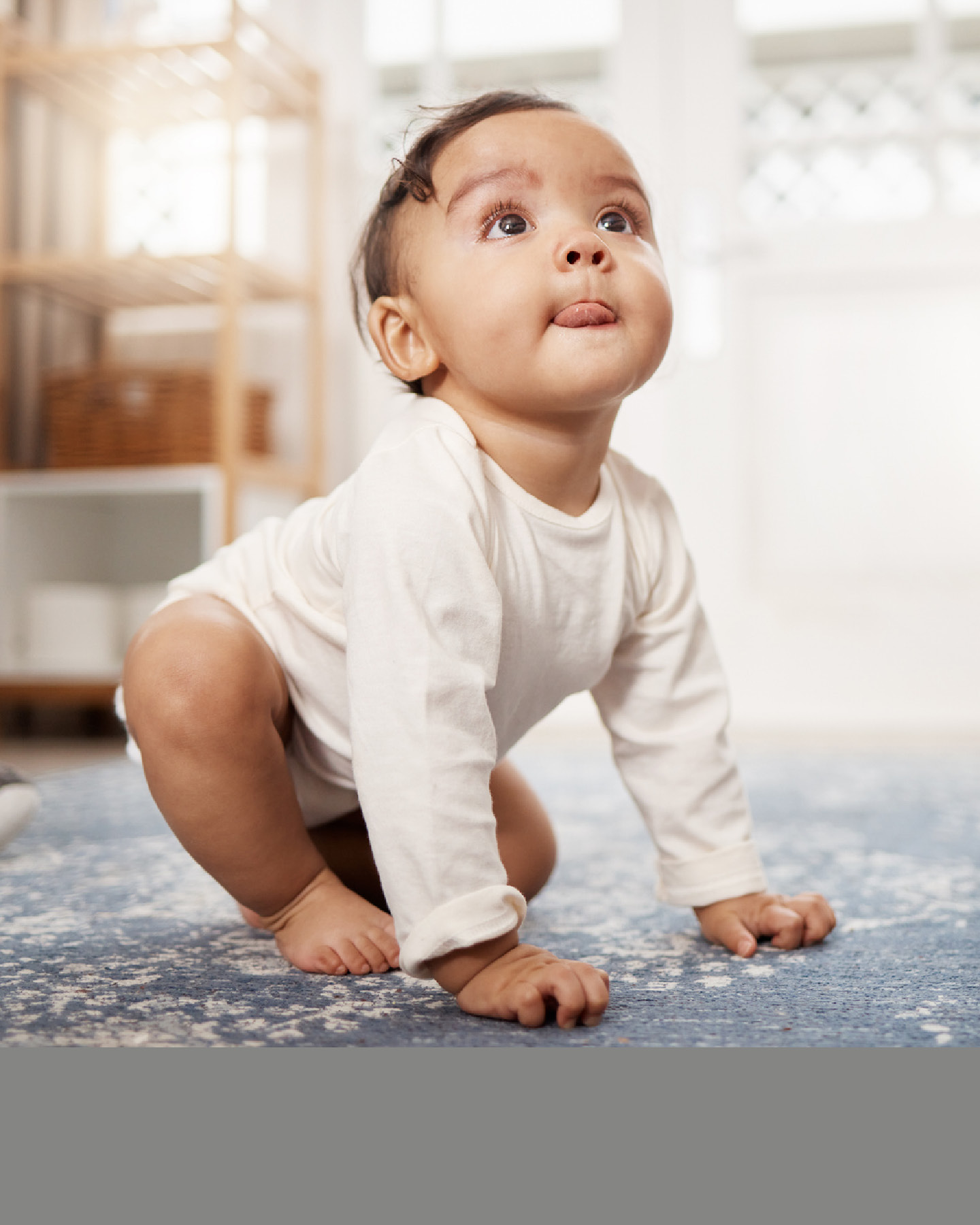 Baby in weißem Body krabbelt auf dem Teppich 