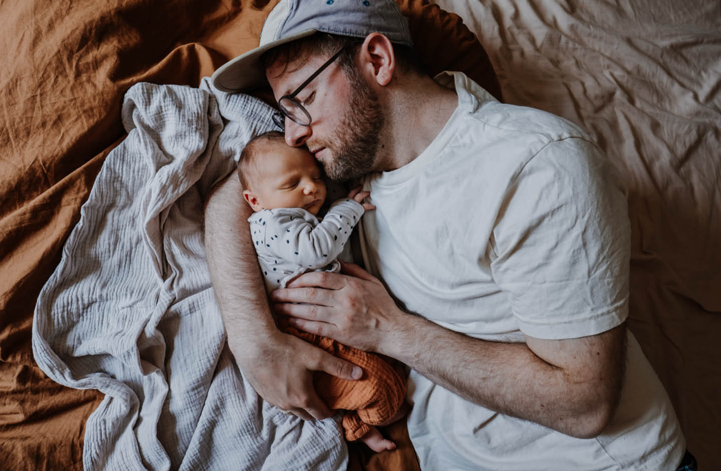 Vater liegt mit Baby auf einer Decke.