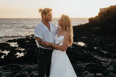 Hochzeitspaar am Strand in sommerlichem Hochzeitsoutfit lächelt sich verliebt an