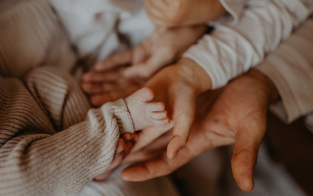 Familie hält mit ihren Händen den Fuß des Neugeborenen liebevoll fest.